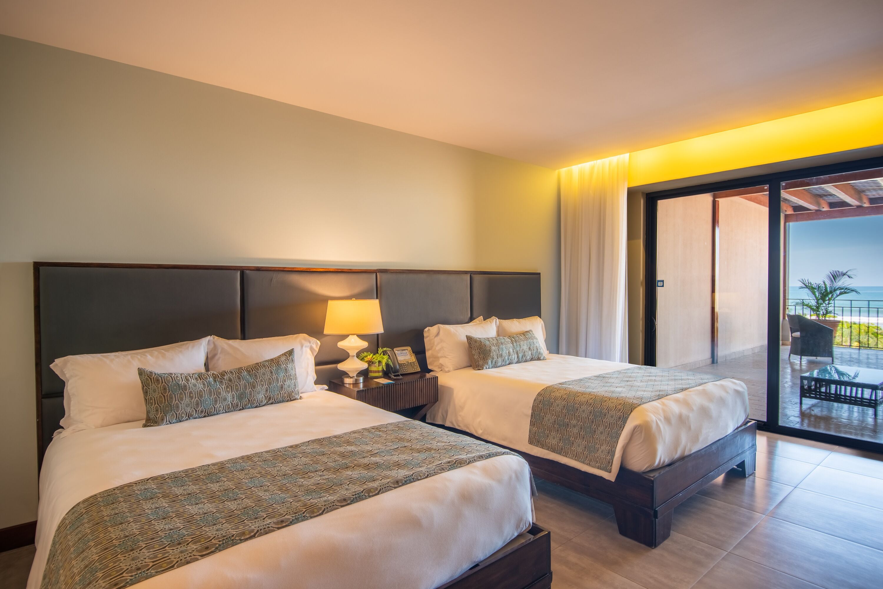 Hotellihuone, jossa on kaksi sänkyä, yöpöytä lampun kanssa ja näkymä ulkoalueelle.