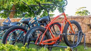 Bicycles parked in an outdoor area with a stone wall and greenery in the background.