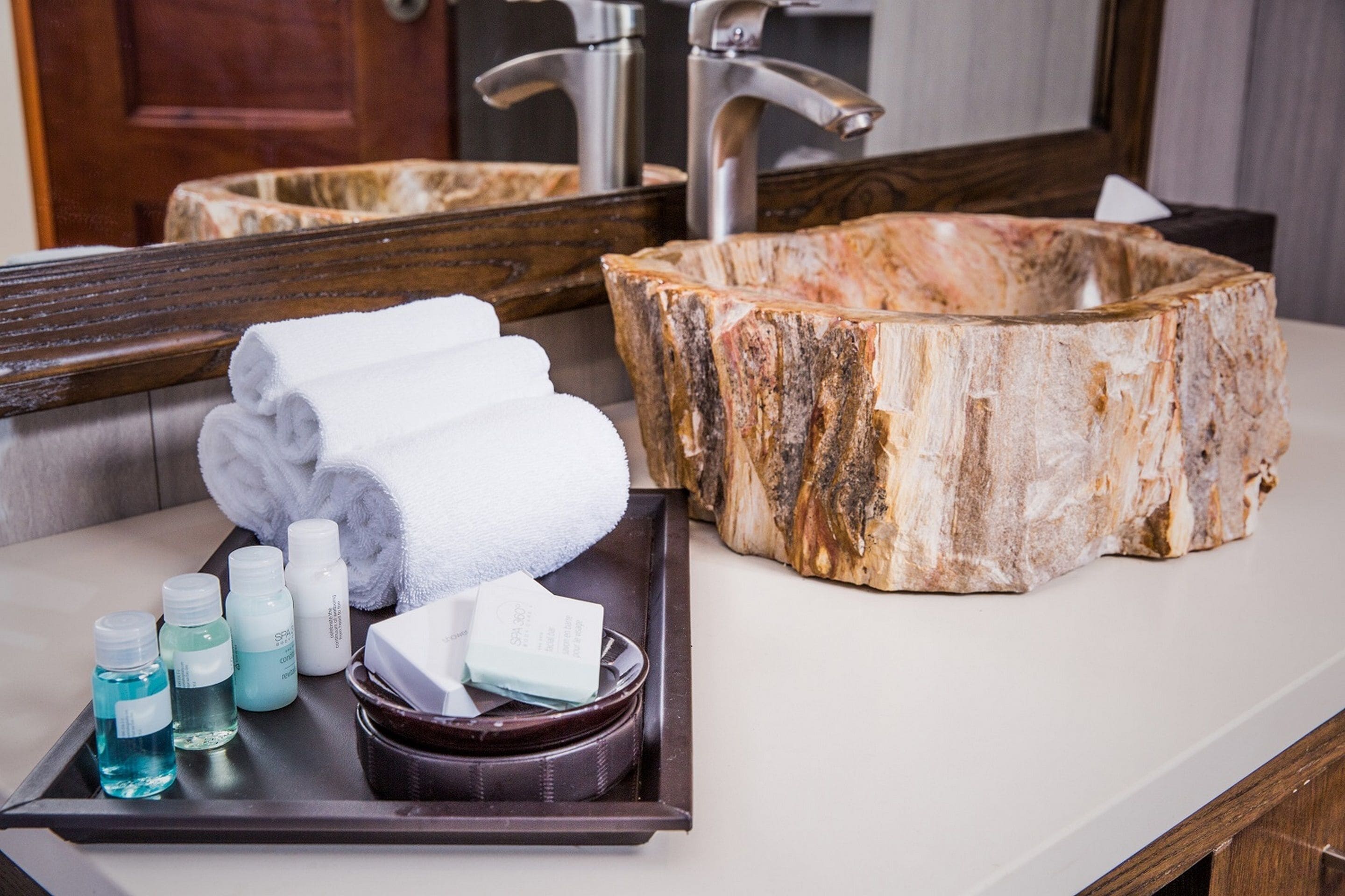 A bathroom vanity with a marble sink, a tray with toiletries, and a mirror.