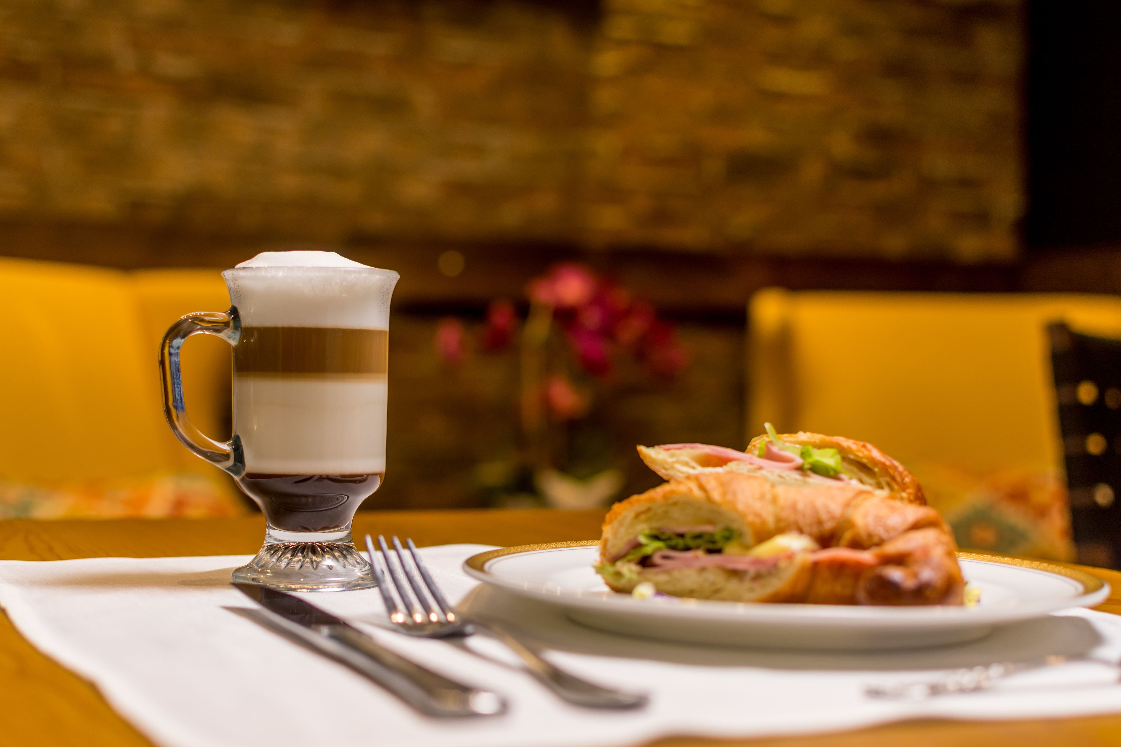 Una mesa con una taza de vidrio, un sándwich y cubiertos sobre un servilleta blanca.