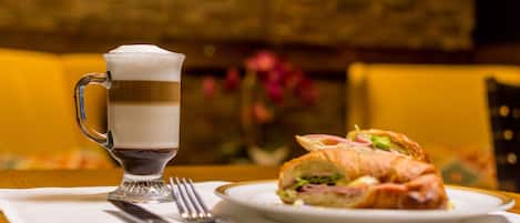 Una mesa con una taza de vidrio, un sándwich y cubiertos sobre un servilleta blanca.