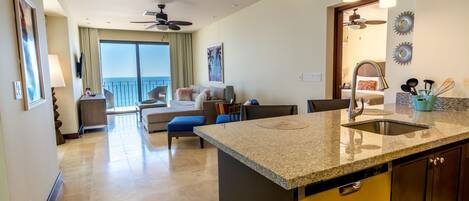 A modern kitchen with granite countertops, a built-in sink, and a dining area with a blue chair.