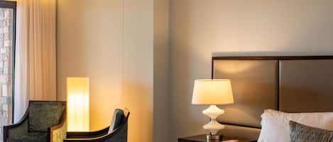 A hotel room with a bed, a nightstand with a lamp, a chair, and a large window with curtains.