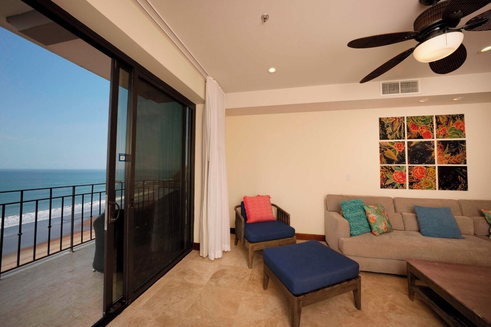 A balcony with a view of the ocean, a sofa with colorful cushions, and a ceiling fan.
