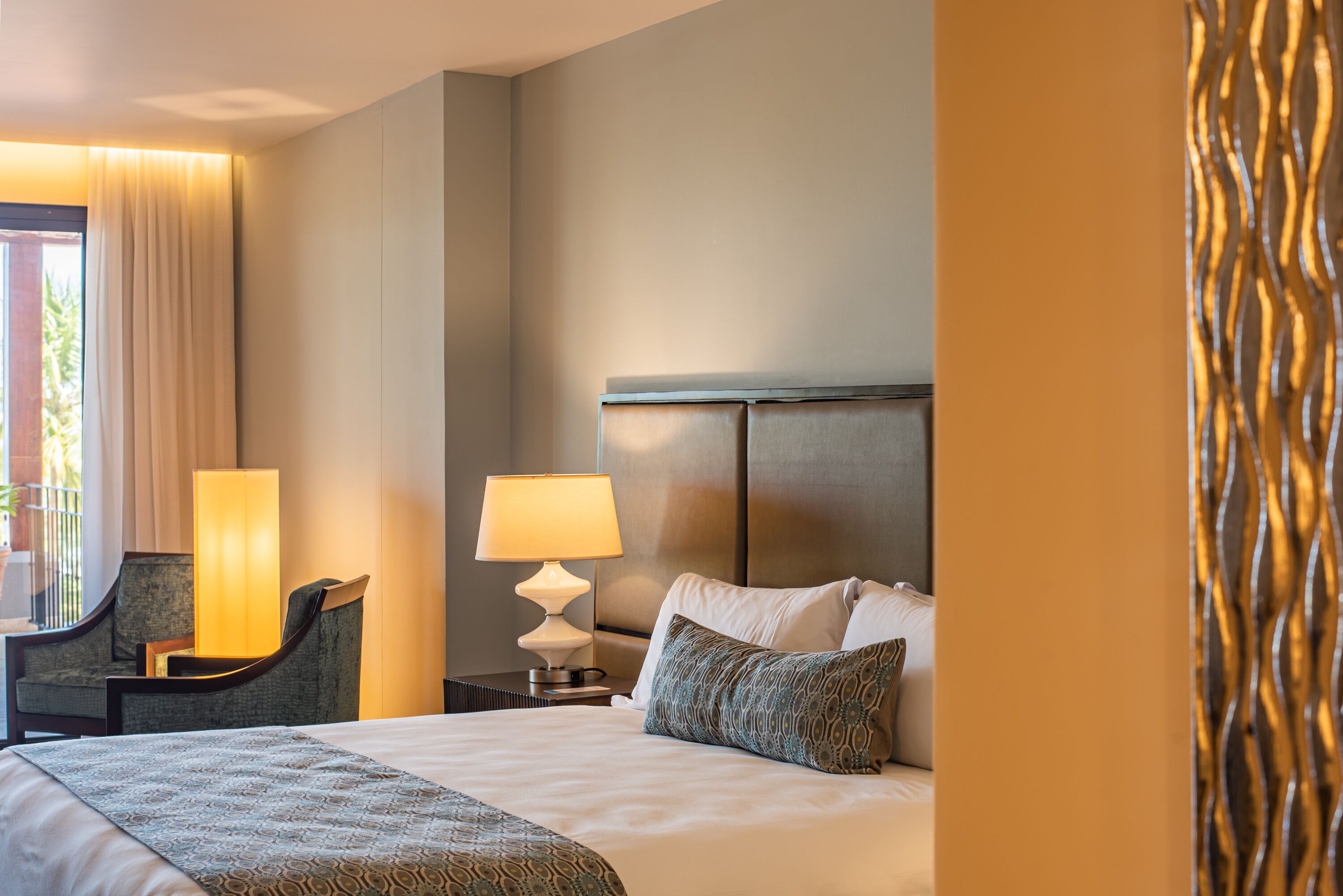 Habitación de hotel con una cama grande, dos lámparas de noche, una silla y vistas al exterior.