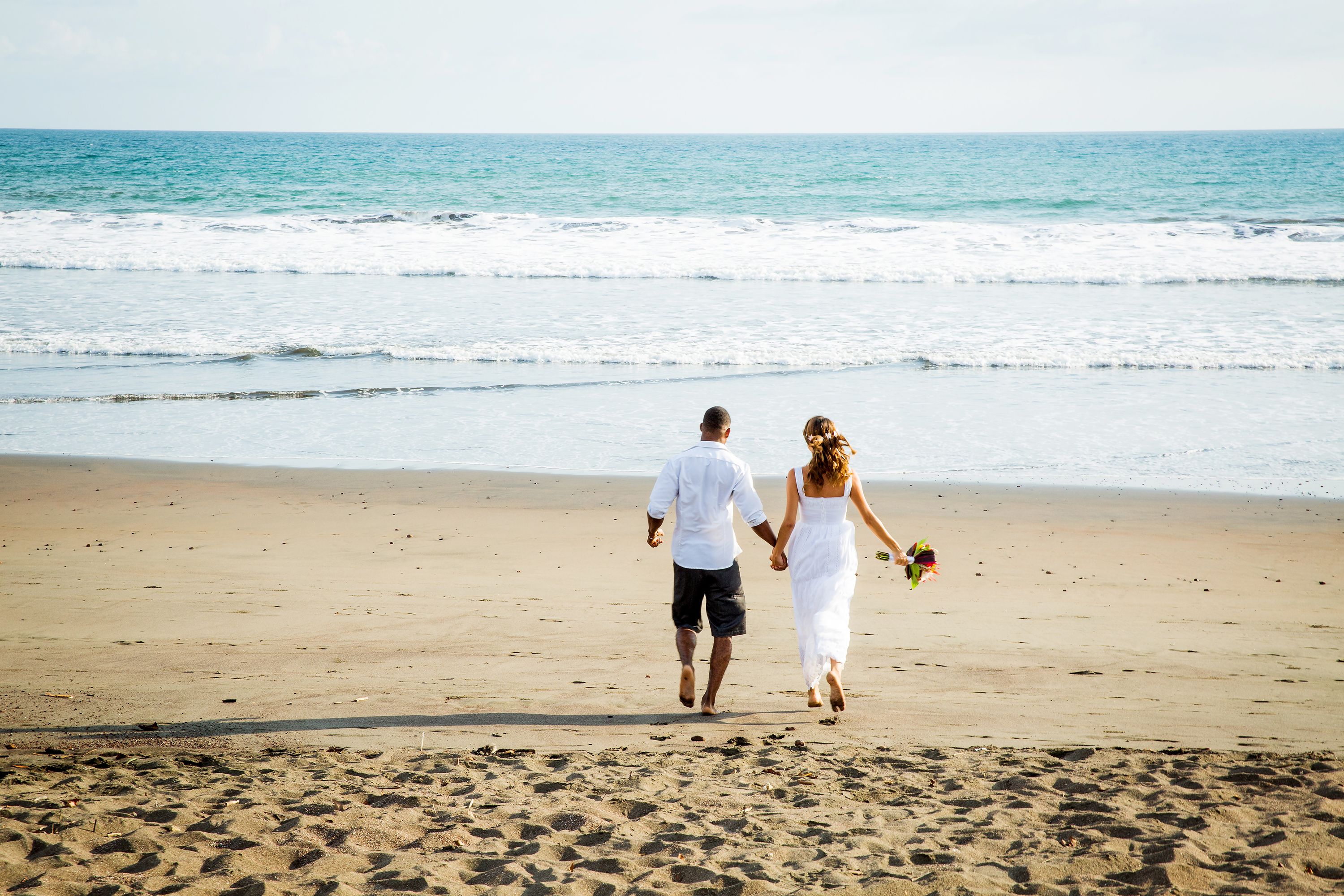 A couple walking on a sandy beach with the ocean in the background.