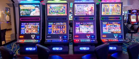 Quatre machines à sous ornées d’enseignes au néon, chacune affichant un titre de jeu différent.