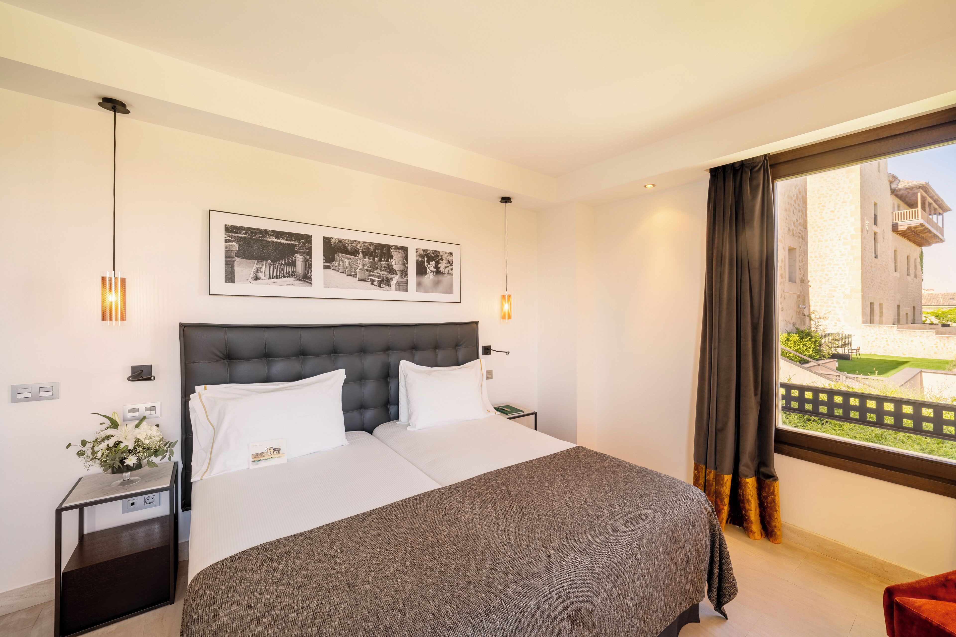 A modern hotel room with a large bed, a nightstand, a bedside table, and a window with curtains.