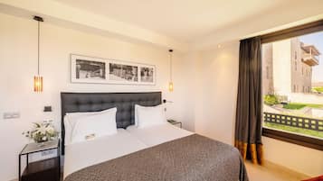 Una habitación de hotel moderna con una cama grande, una mesita de noche y un ventanal con cortinas.
