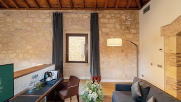 A cozy room with stone walls, a wooden ceiling, a desk with a coffee maker, a sofa, and a lamp.