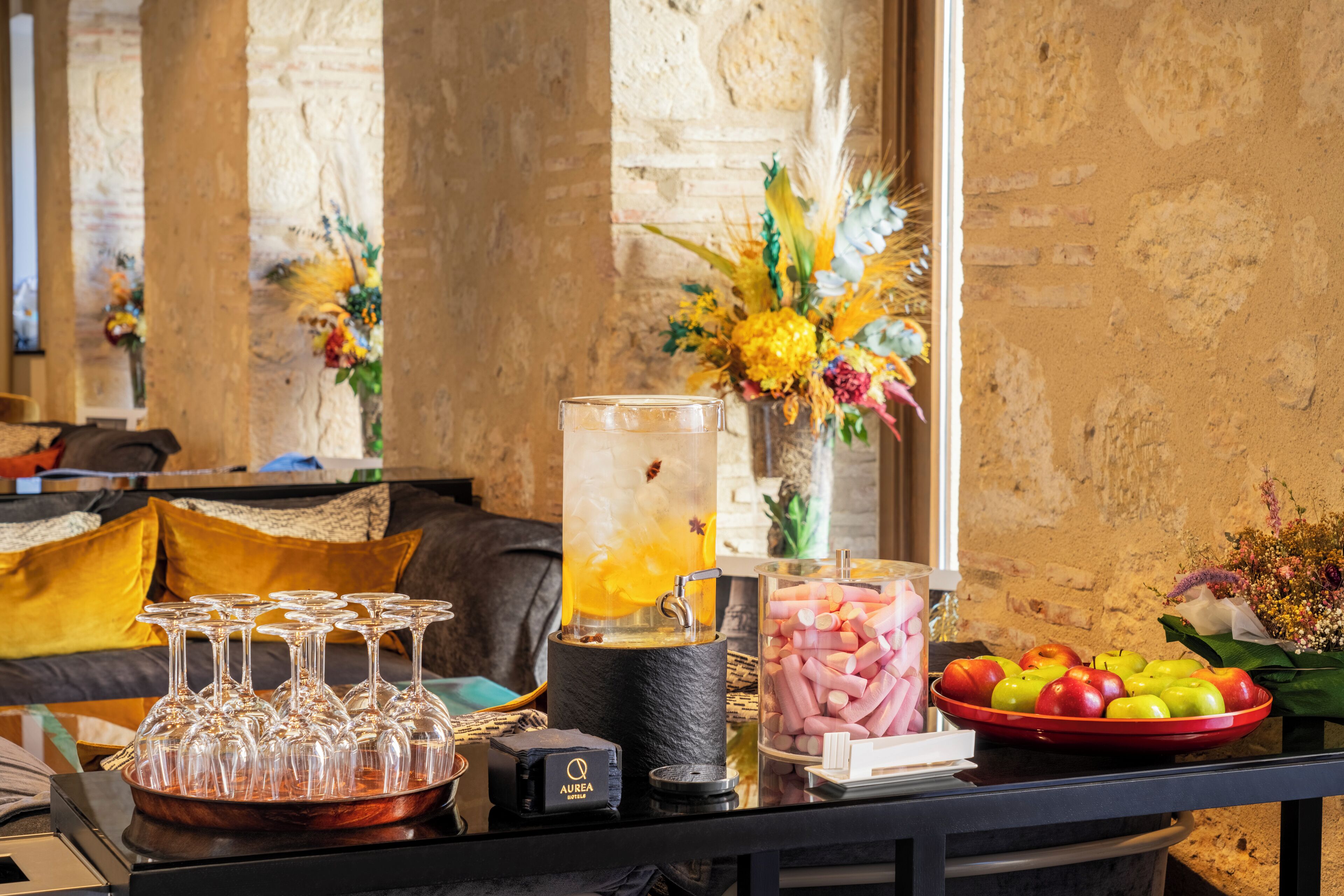 Uma área de bar com dispensador de bebidas, copos e uma cesta de frutas.