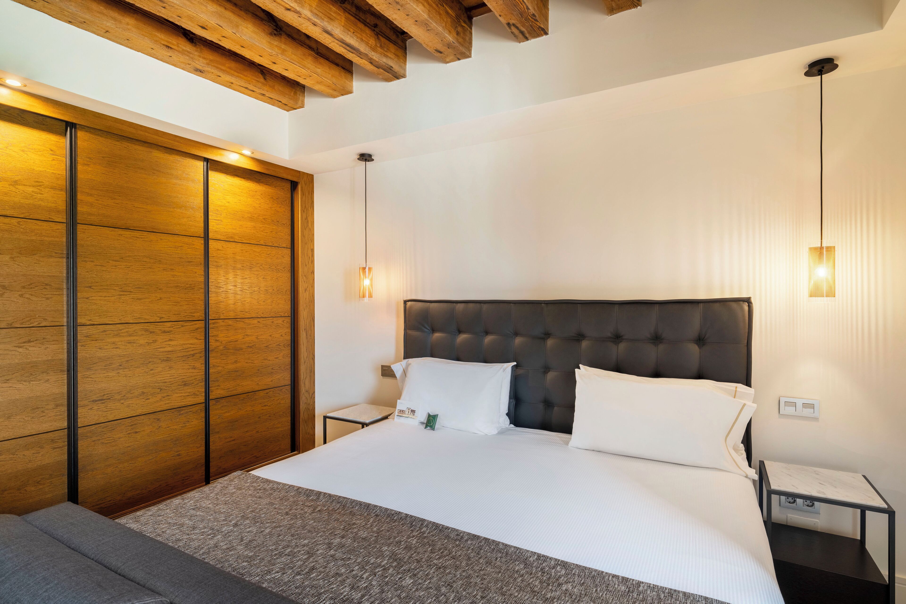 Una habitación de hotel moderna con una cama grande, un armario de madera y una mesita de noche pequeña.