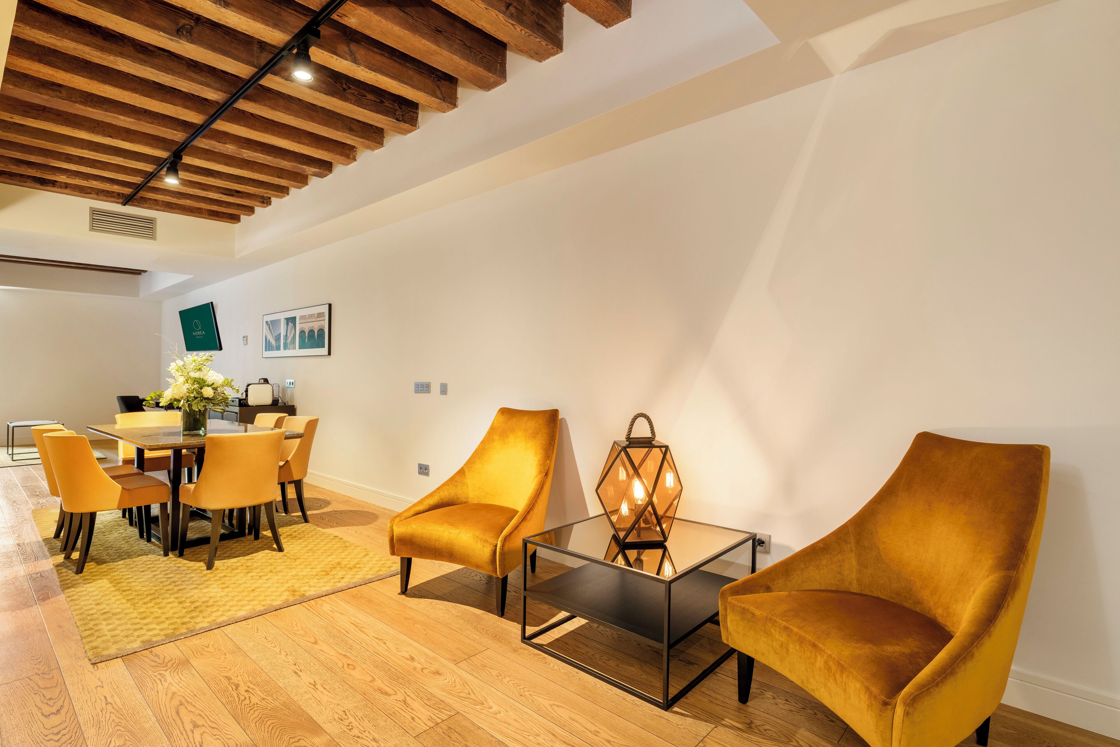 A modern living room with a wooden ceiling, a dining area with yellow chairs, and a glass coffee table.