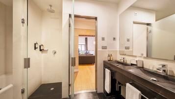 Un baño moderno con ducha envuelta en vidrio, lavamanos de mármol oscuro y un espejo grande.