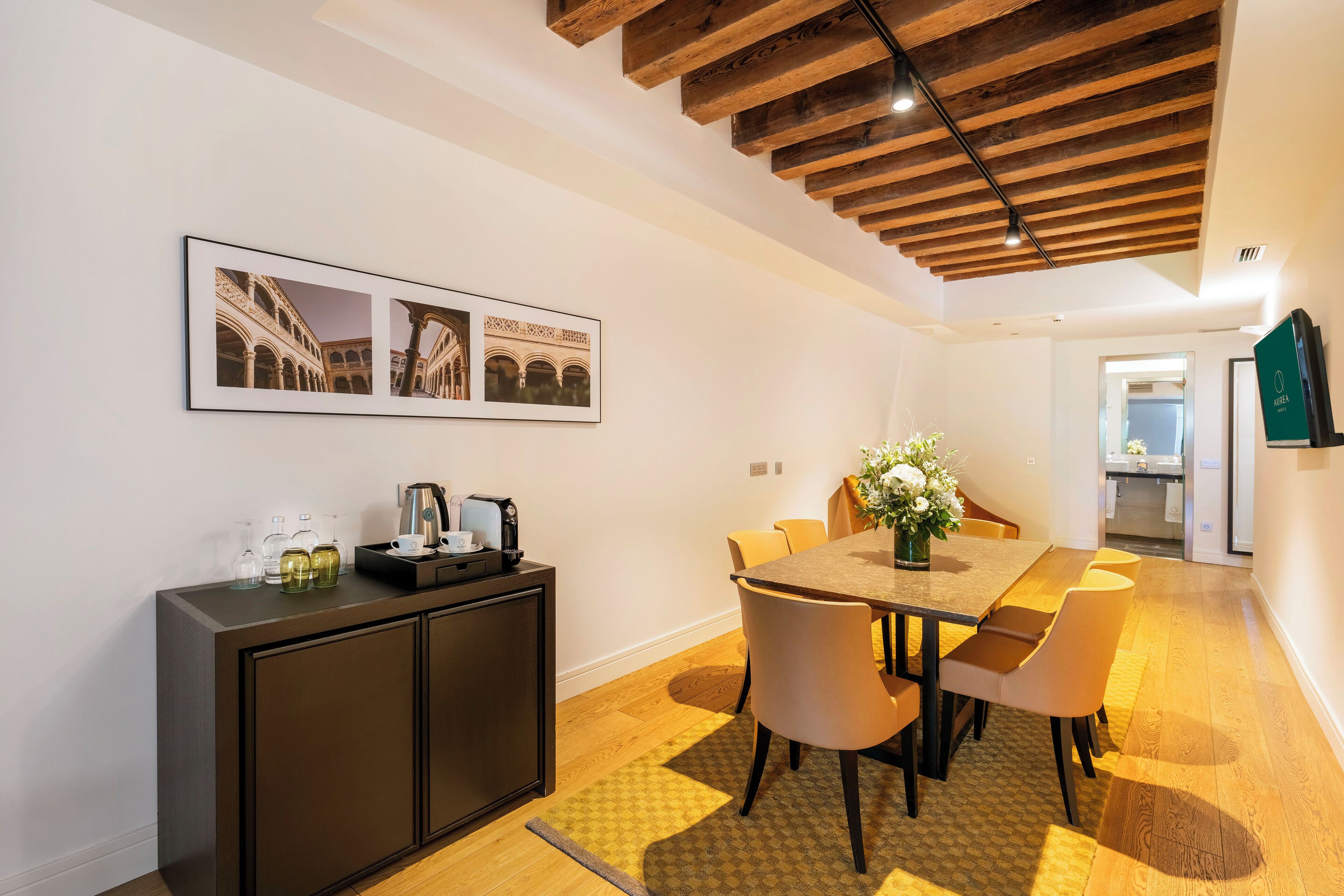 Un comedor con techo de madera, una mesa con sillas, una estación de café y cuadros en la pared.
