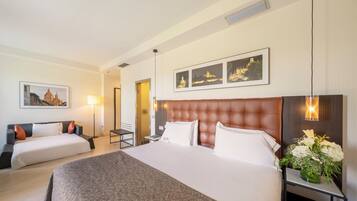 Habitación de hotel con una cama grande, una cama más pequeña, una mesita de noche con un florero, una lámpara y cuadros en la pared.