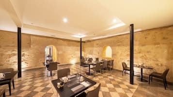 Un espace repas avec un sol à carreaux, des tables, des chaises et un mur en pierre en arrière-plan.