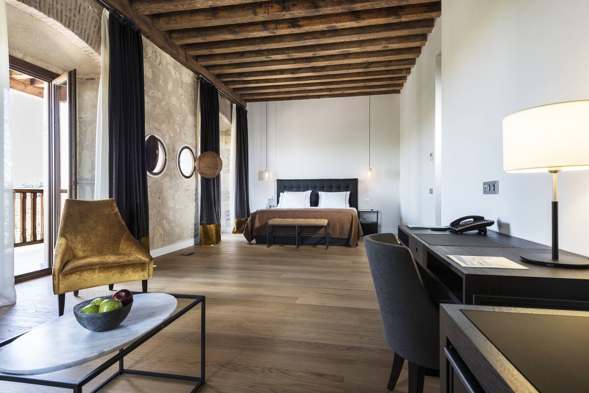 Een hotelkamer met een bed, een bureau, een stoel, een schaal fruit en een lamp.