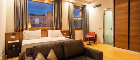 A hotel room with a large bed, a sofa, a chair, and a wardrobe.