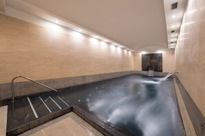 A modern indoor pool with a clear water surface, a tiled floor, and a stone wall.