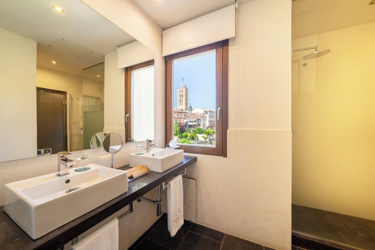 Een moderne badkamer met twee wastafels, een grote spiegel en een raam met uitzicht op een toren.