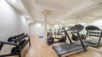 Un gimnasio moderno con cintas de correr, elípticas y un estante con mancuernas.