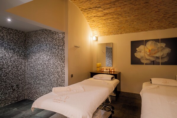 Un cuarto de spa con dos camillas de masaje, una zona de ducha y un espejo montado en la pared.