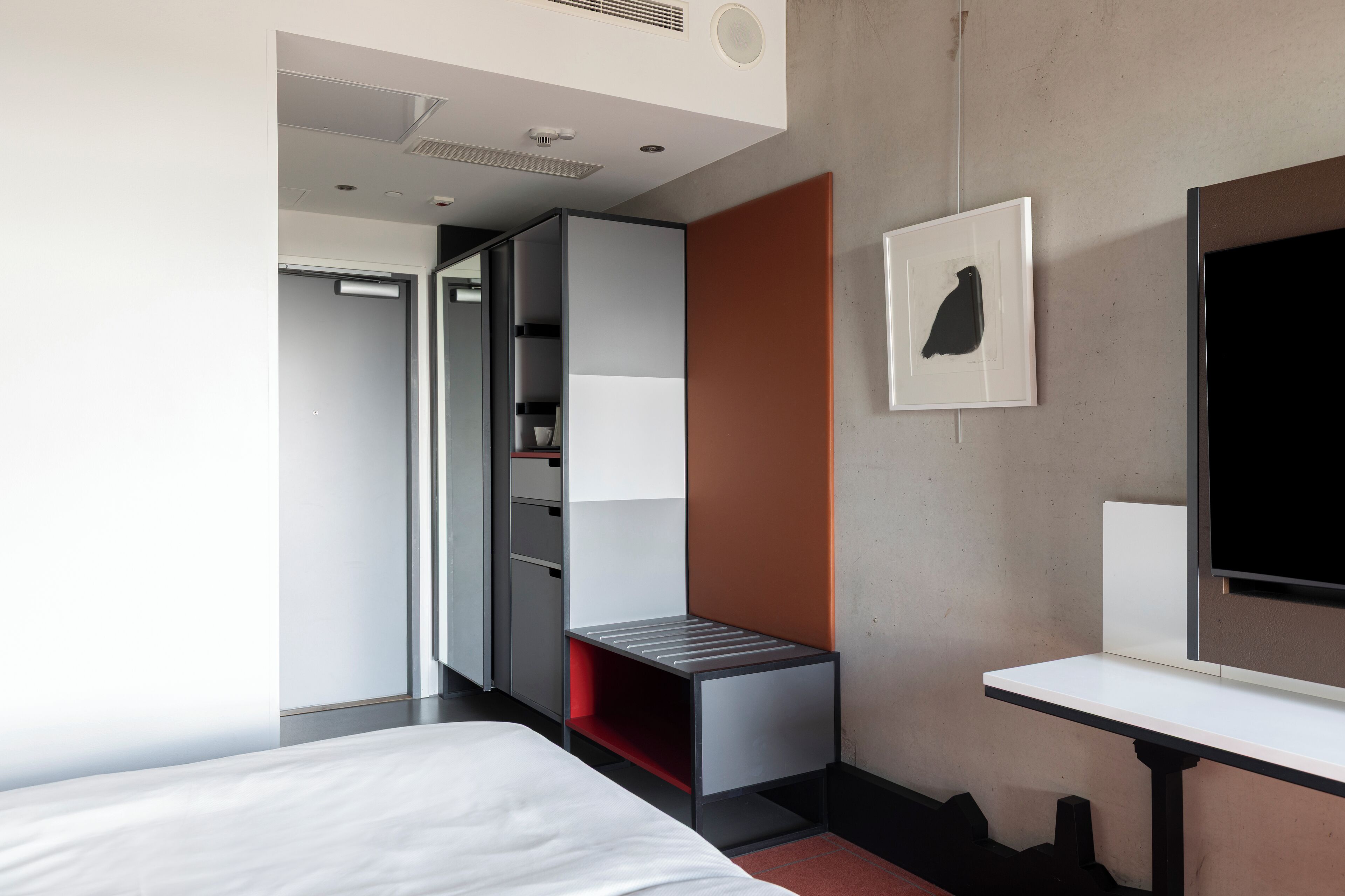 A modern hotel room with a bed, a desk, a wardrobe, and a television.
