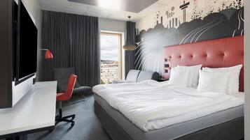 Una habitación de hotel moderna con una cama grande, un escritorio, una silla y vistas a la ciudad a través del ventanal.