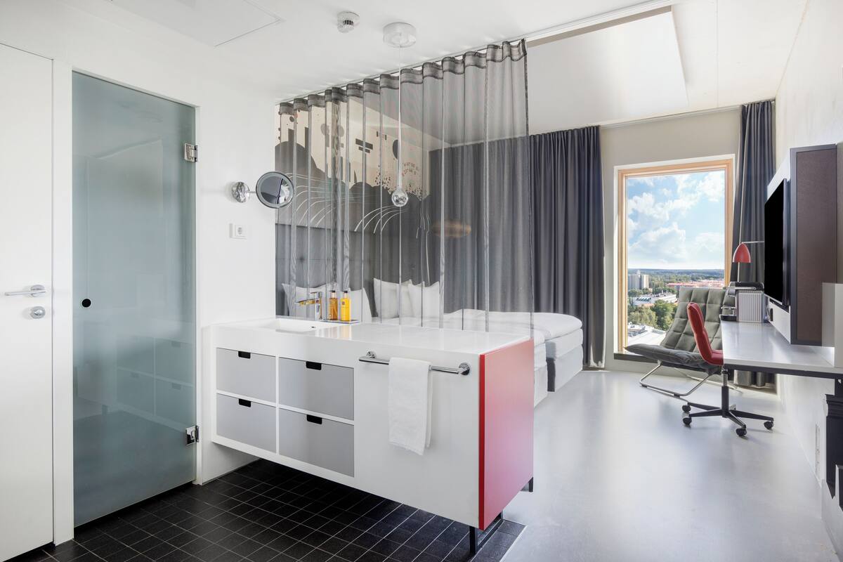 Ein modernes Hotelzimmer mit großem Fenster, einem privaten Balkon, einem Schreibtisch mit Stuhl und einem großen Spiegel.