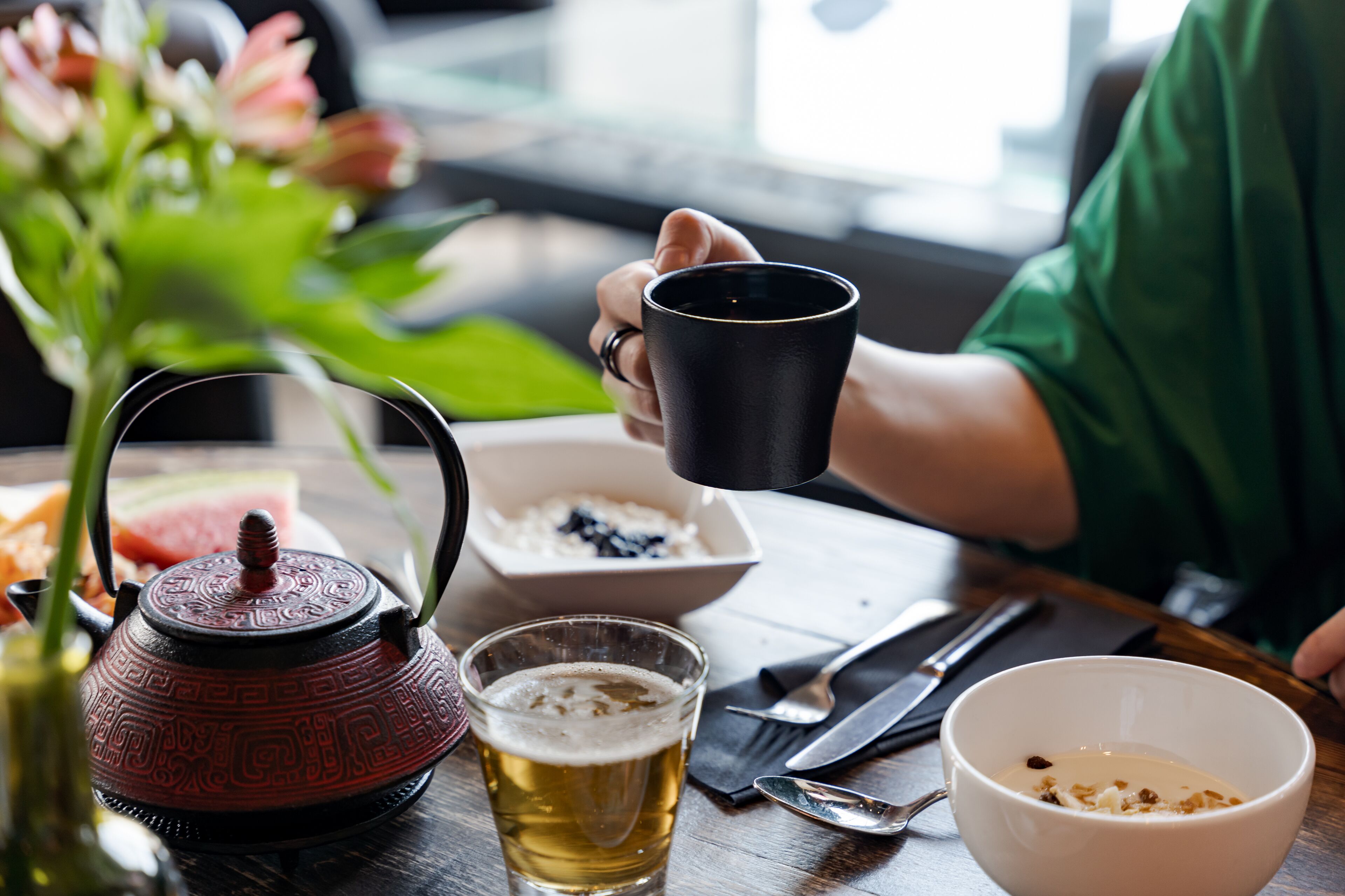 A table with a teapot, a glass of beer, a bowl of cereal, and a cup of coffee.