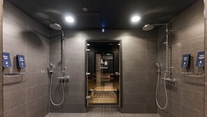 Área de chuveiro moderna com duas cabeças de chuveiro, um banco e uma placa indicando uma sauna.