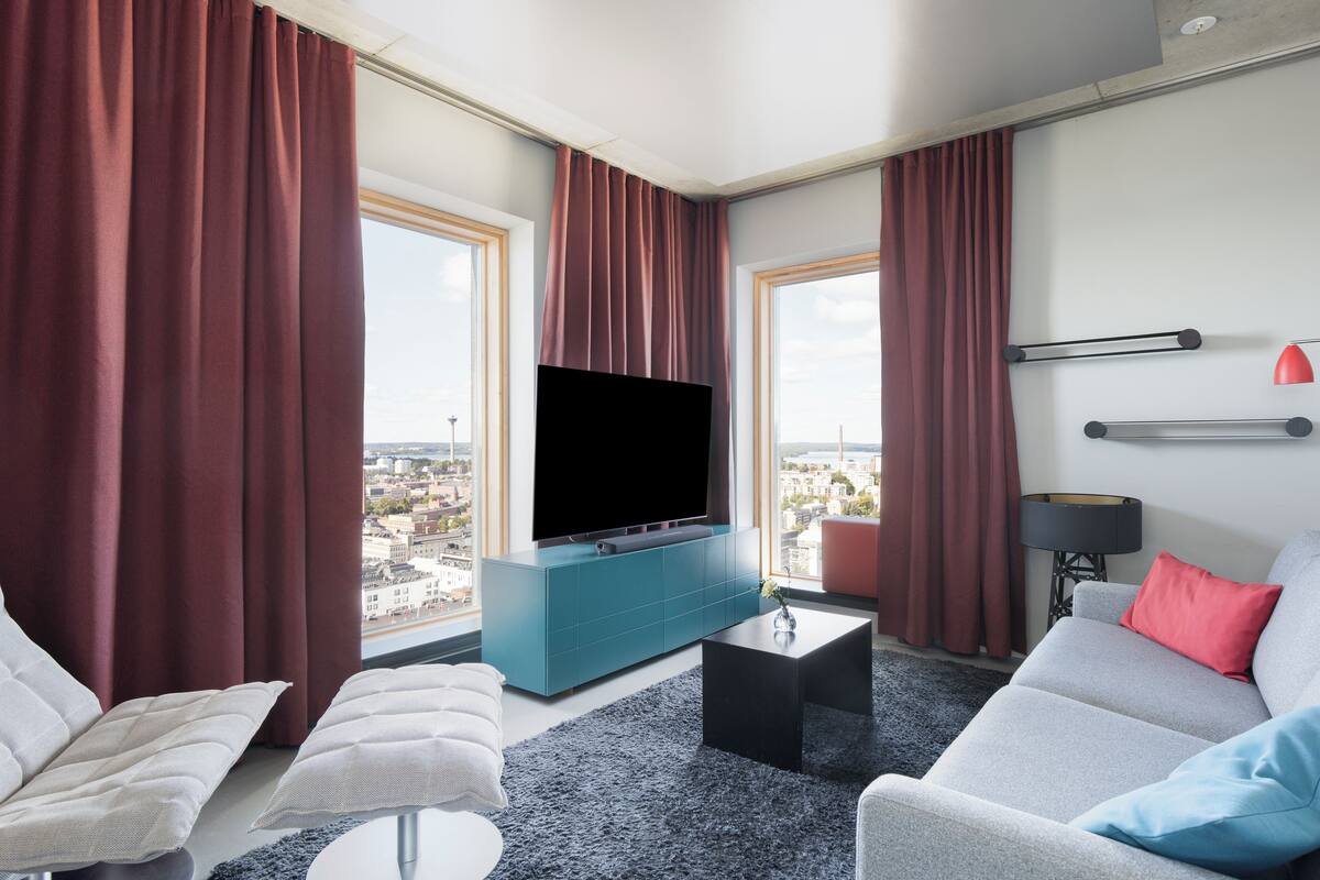 A modern living room with a large flat-screen TV, teal accent wall, and a city view.