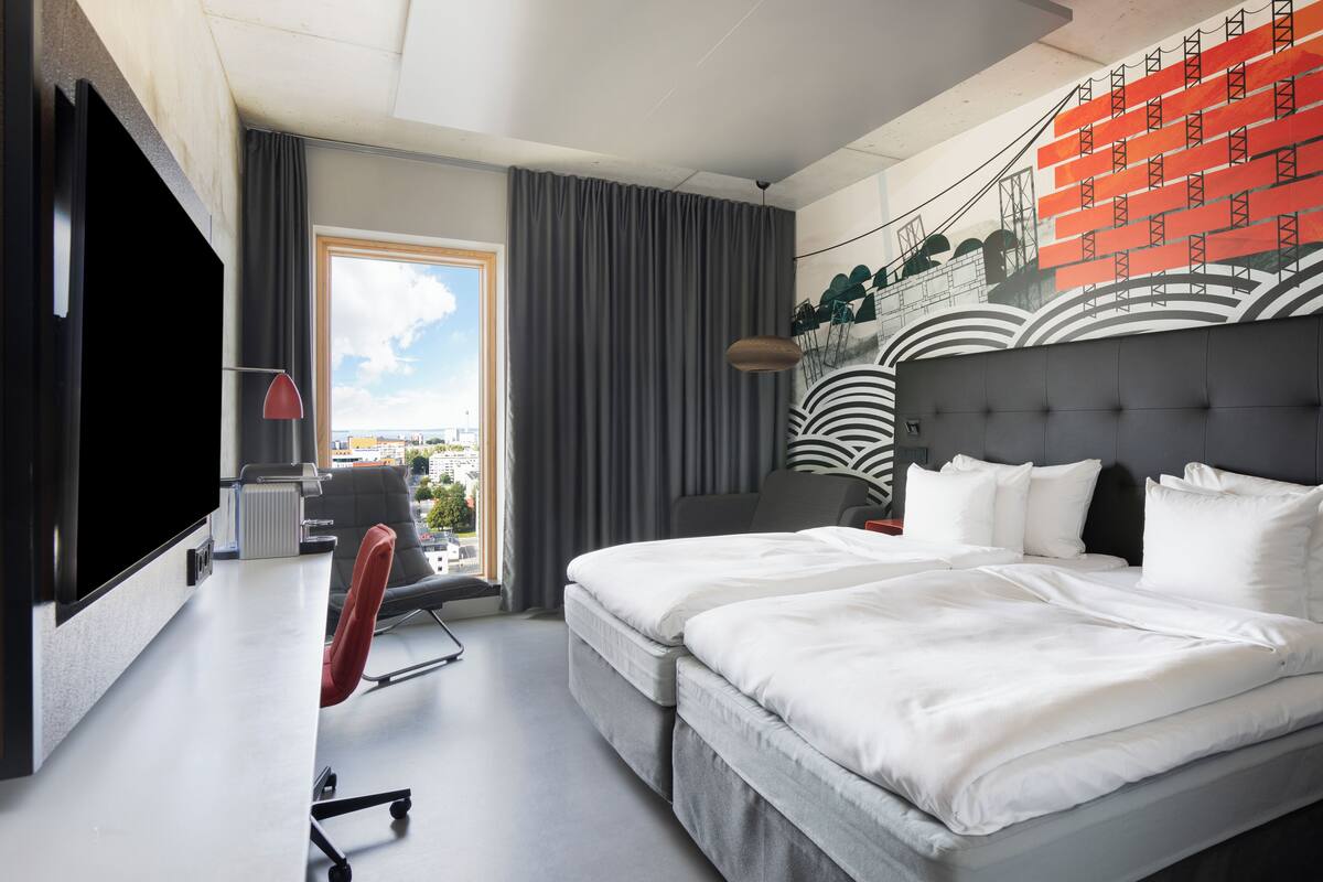 A modern hotel room with a large bed, a desk, a chair, and a TV.