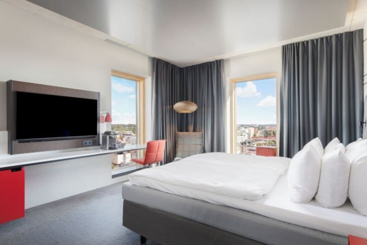 A hotel room with a bed, a TV, a desk, and a view of the city.