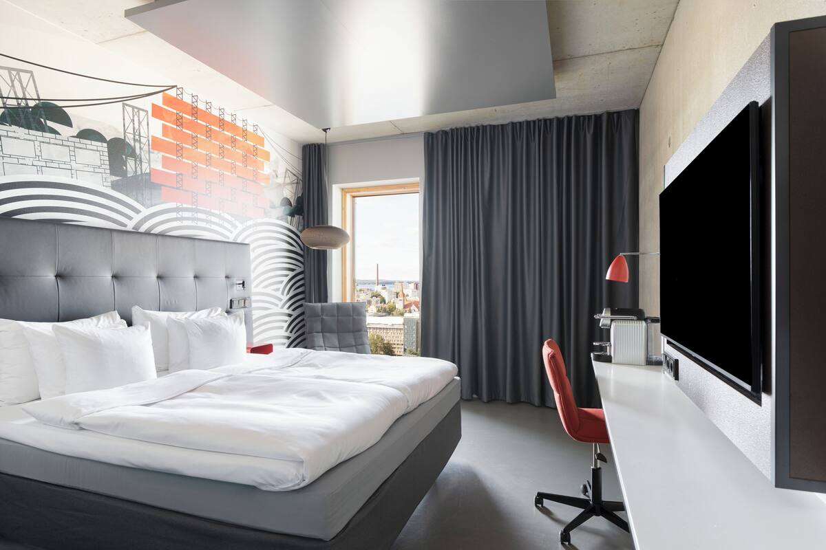 Ein modernes Hotelzimmer mit einem großen Bett, einem Schreibtisch, einem Fernseher und Blick auf die Stadt.