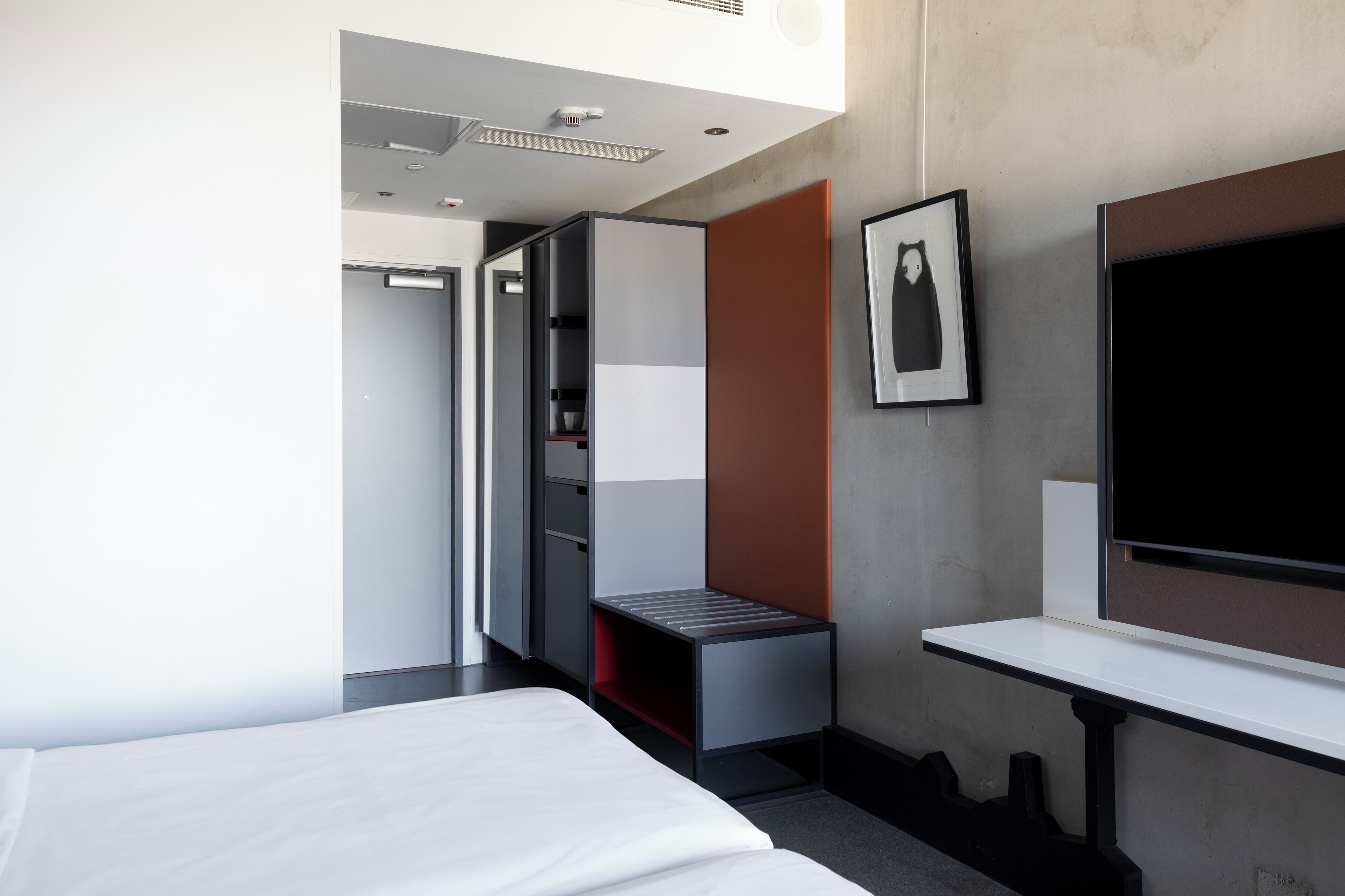 Moderni hotellihuone, jossa on sänky, työpöytä, vaatekaappi ja televisio.