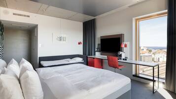 A hotel room with a bed, a desk, a chair, a TV, and a large window with a city view.