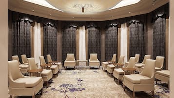 Un salón de conferencias con filas de sillas y mesas color beige, una alfombra estampada y un techo con una lámpara central.