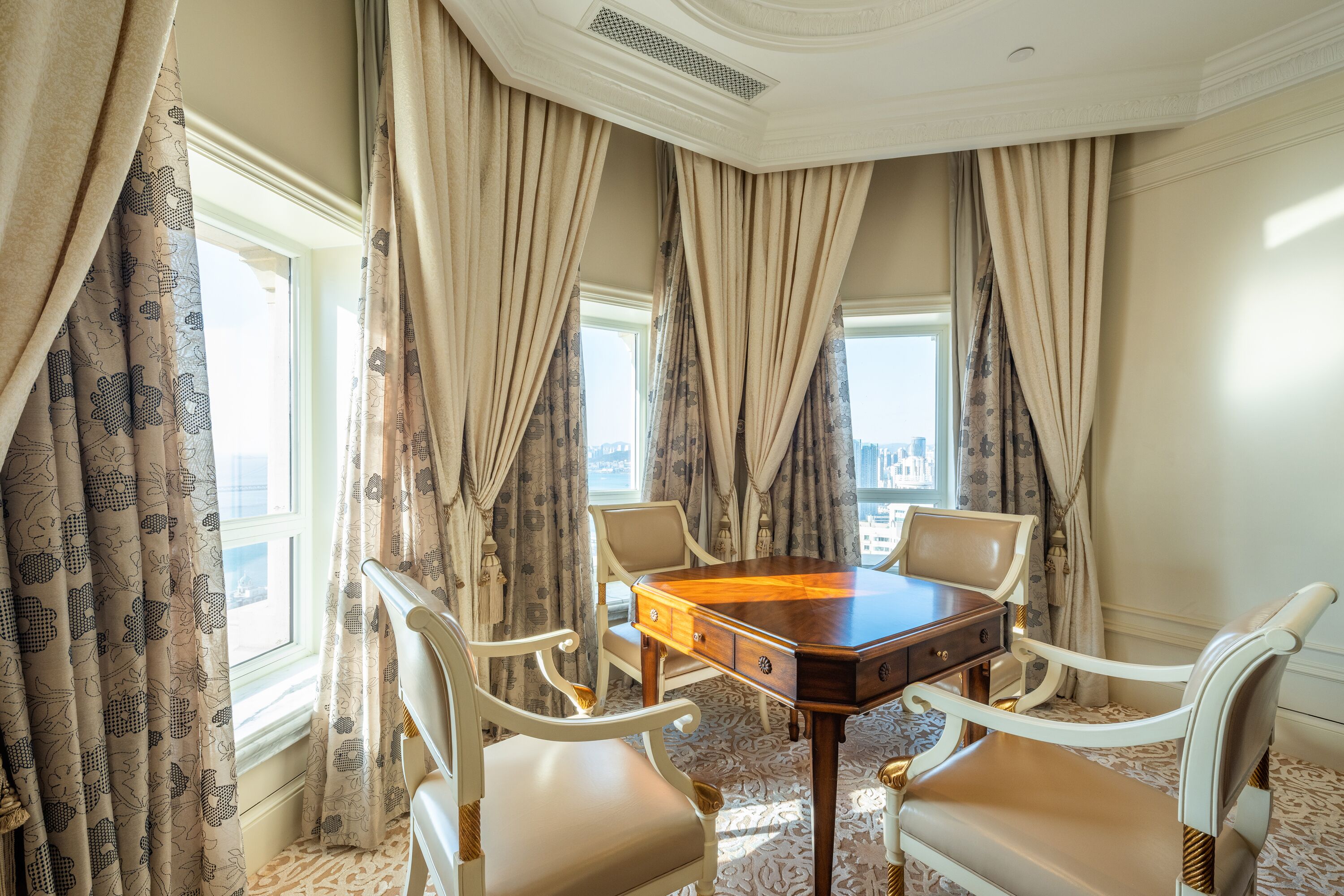 A conference room with a wooden table, four chairs, and large windows with curtains.