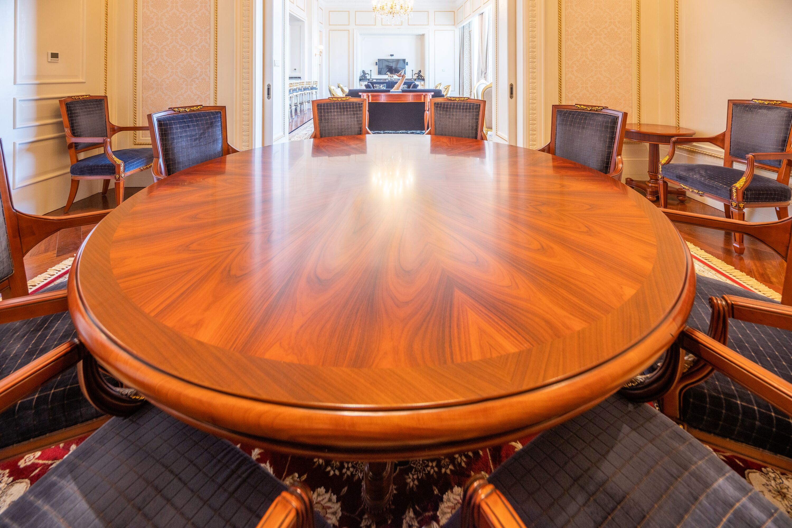 A conference room with a large wooden table surrounded by chairs, a television, and a patterned carpet.