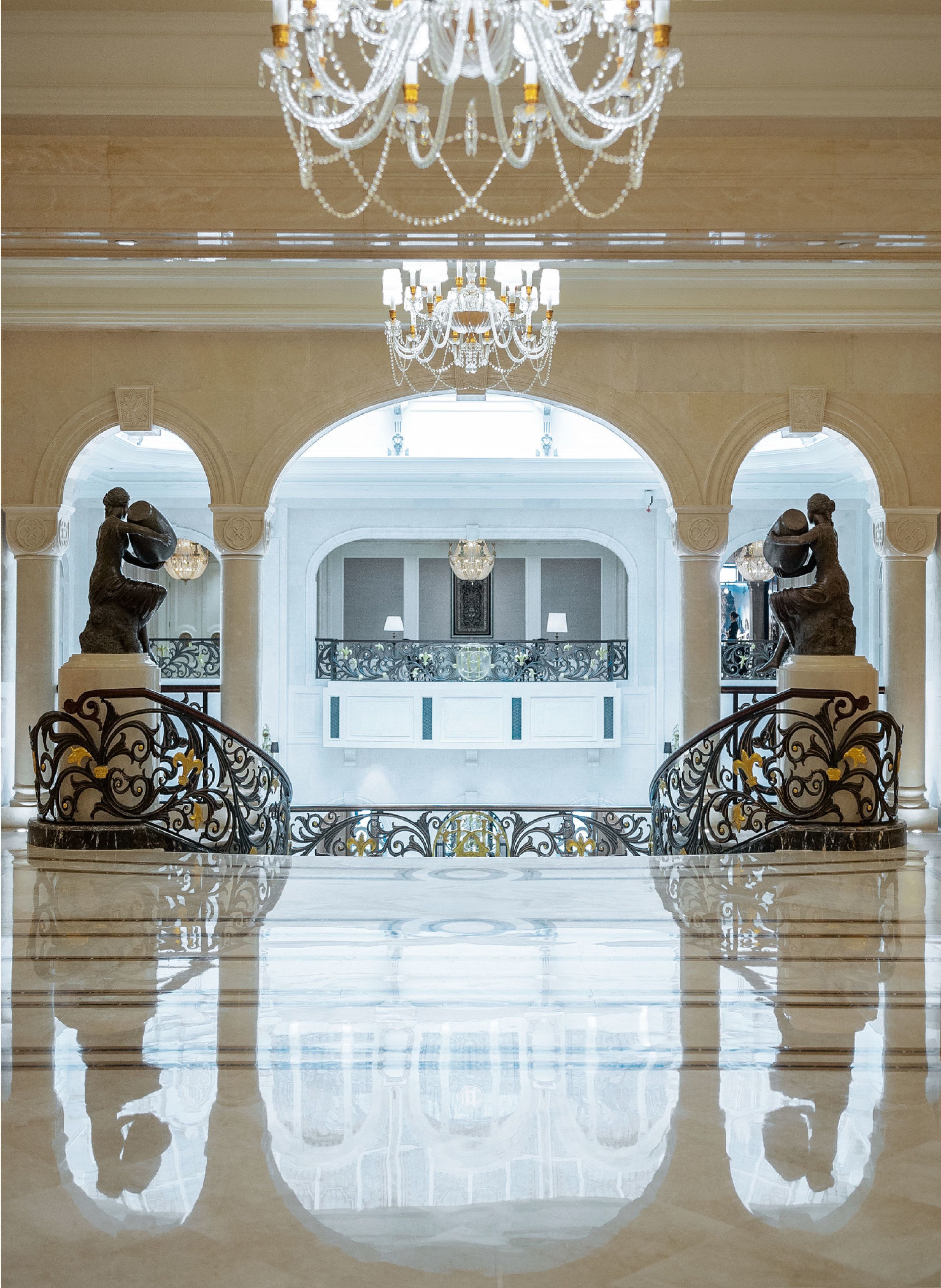 Un vestíbulo imponente con piso reflectante, candelabros ornamentales y estatuas a cada lado de una recepción central.