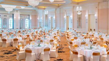 Un gran salón de banquetes con mesas redondas, manteles blancos y fajas doradas.