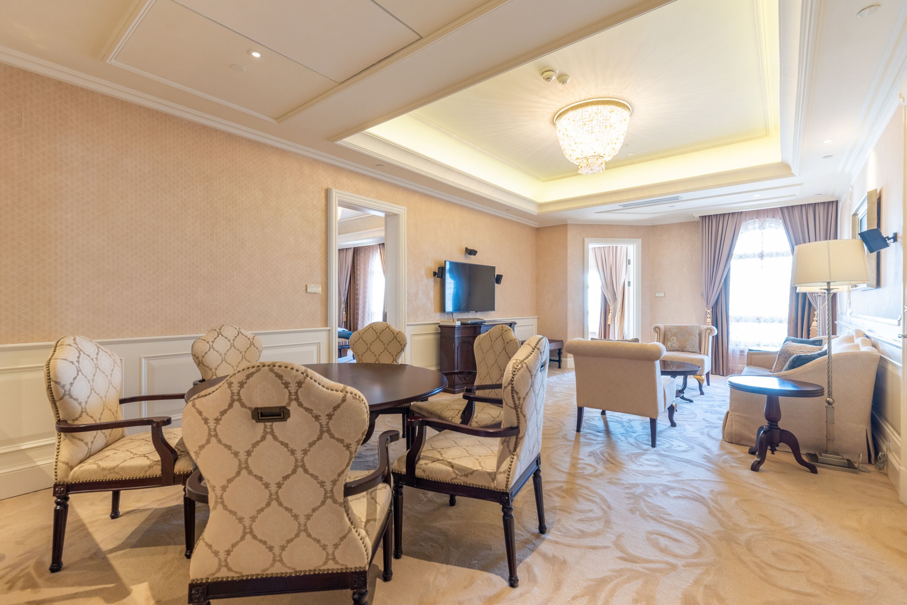 A hotel room with a dining area, a television, and a chandelier.