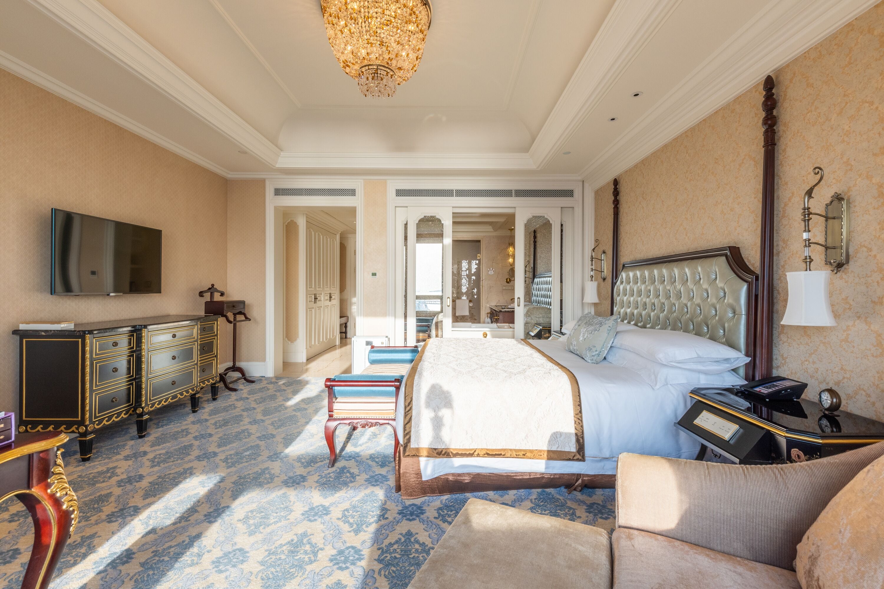 A hotel room with a large bed, a television, a dresser, and a chandelier.