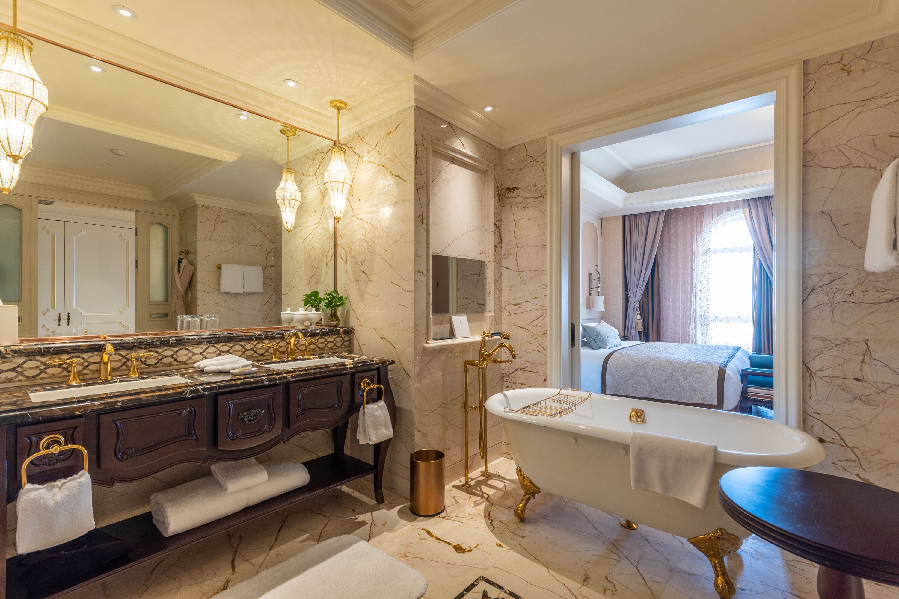 A luxurious bathroom with a marble floor, a freestanding bathtub, a vanity with gold fixtures, and a large mirror.