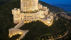 A large, castle-like hotel with multiple towers and a well-lit facade, surrounded by lush greenery and a coastal backdrop. - The Castle Hotel, a Luxury Collection Hotel, Dalian (Dalian)