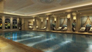 A large indoor swimming pool with a tiled floor, surrounded by lounge chairs and tables, and decorated with plants and wall art. - The Castle Hotel, a Luxury Collection Hotel, Dalian (Dalian)