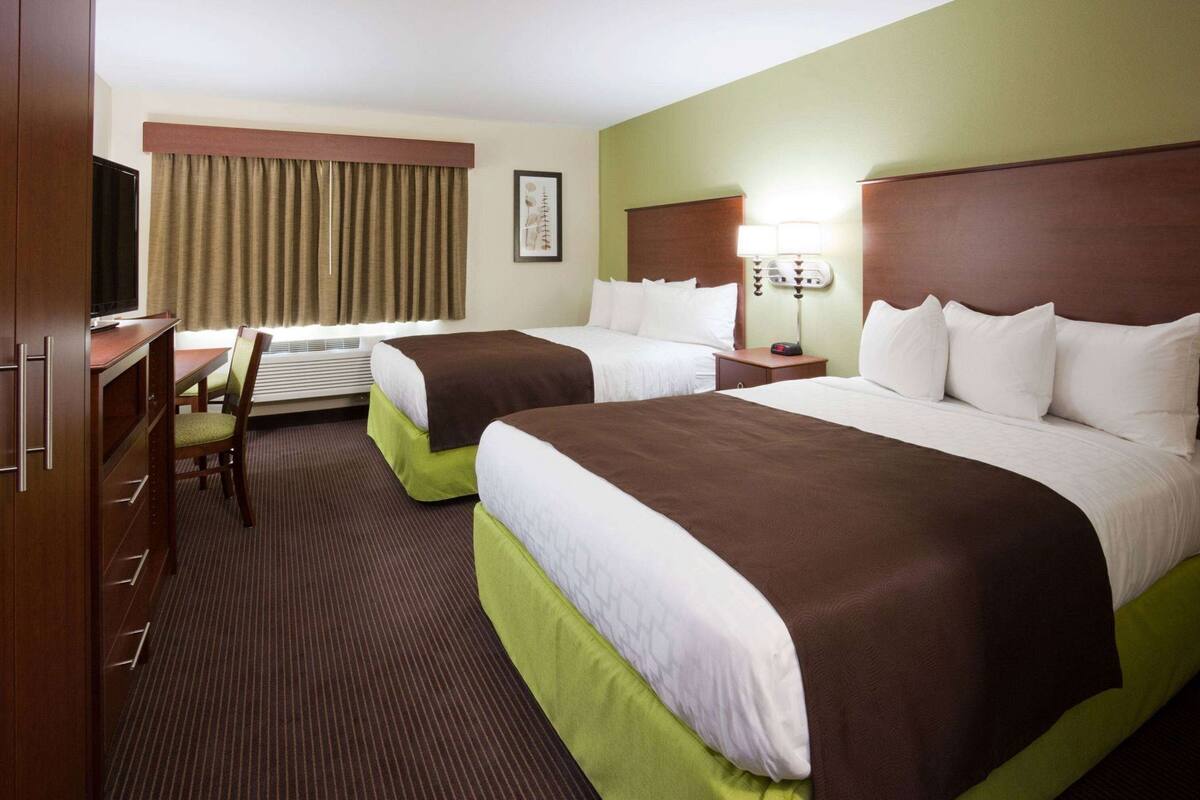 Habitación de hotel con dos camas, un escritorio, una silla, un televisor y una ventana con cortinas.