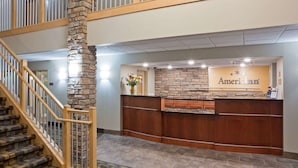 A reception area with a stone pillar, wooden reception desk, and a staircase. - AmericInn by Wyndham Hawley (Hawley)
